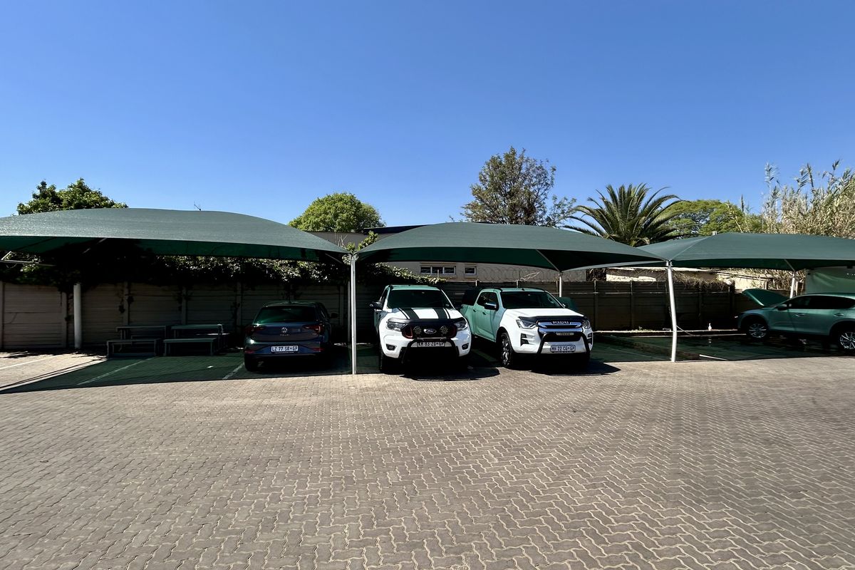 A paved commercial parking area featuring multiple shade cloth carports and a secure perimeter wall.