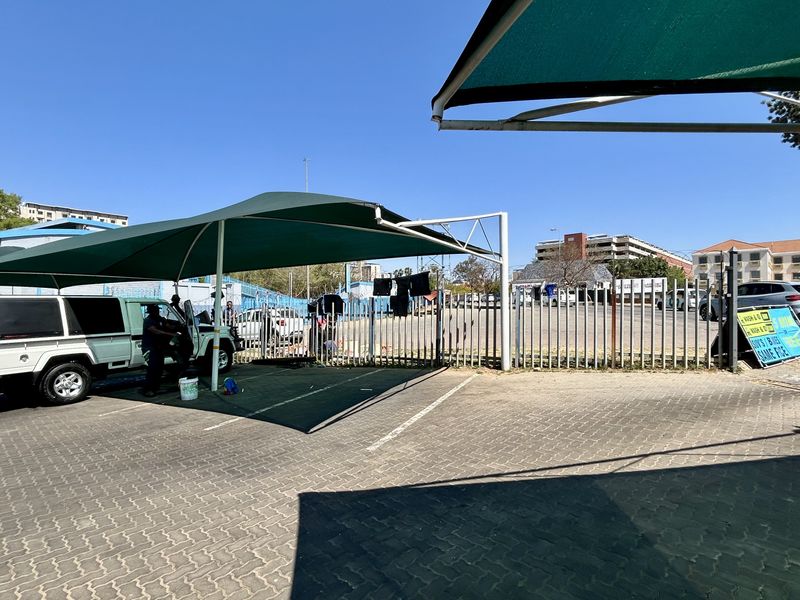 Commercial vacant land featuring a paved parking area with shade cloth carports and secure steel perimeter fencing.