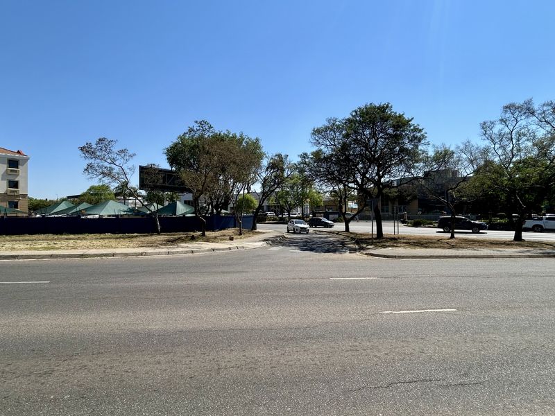 A street-level view of the commercial property frontage, showing access from the main road, mature trees, and existing signage.