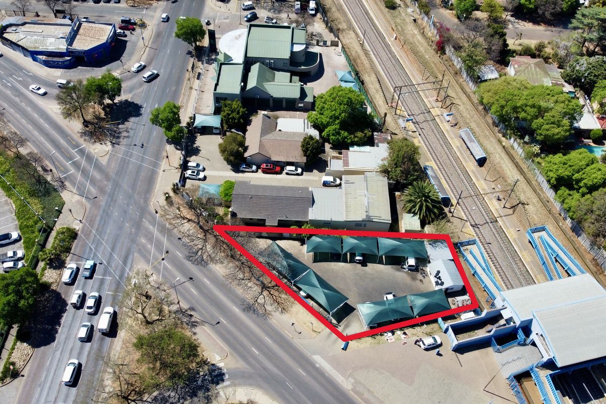 Aerial view of a commercial vacant land plot featuring a paved parking area with installed shade cloth carports, situated near a main road.