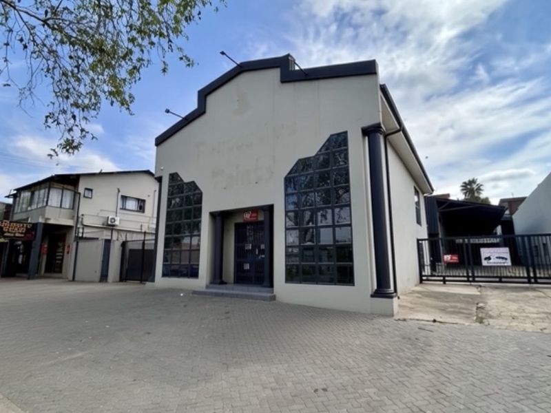 Front elevation of an industrial property featuring a paved driveway, secure gated access, and large glass windows with decorative columns.