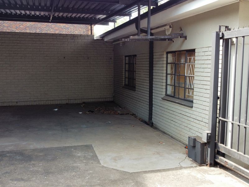 A covered industrial garage area featuring concrete flooring, brick walls, and a secure metal gate entrance.