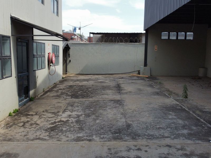 Rear industrial yard area featuring concrete paving, perimeter wall with security fencing, and a covered loading or storage section.