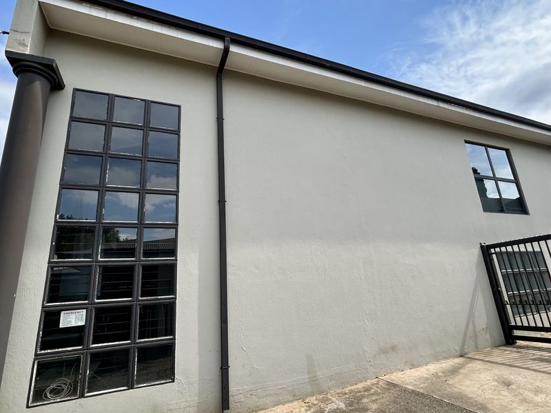 Rear exterior view of the industrial building featuring grid-pattern windows, a security gate, and concrete paving.