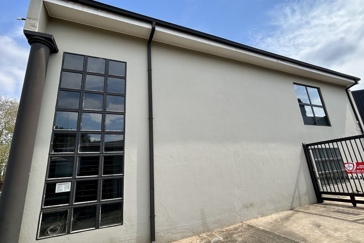 Rear exterior view of the industrial building featuring grid-pattern windows, a security gate, and concrete paving.
