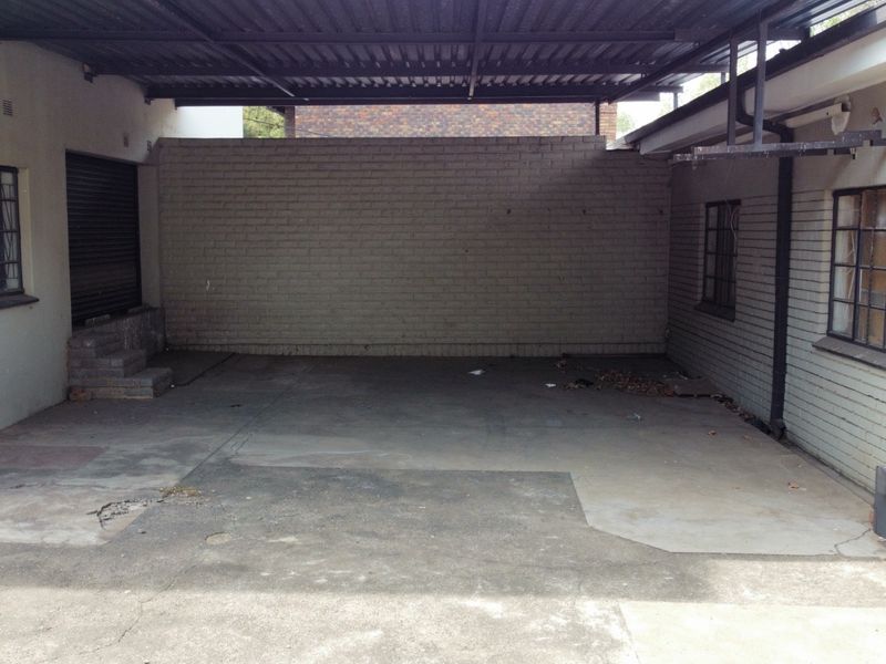 A covered industrial garage or loading area featuring concrete flooring, brick walls, and security bars on windows.