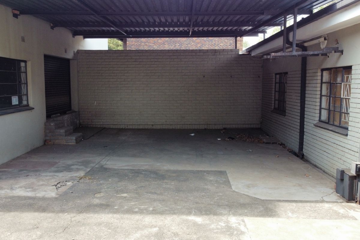 A covered industrial garage or loading area featuring concrete flooring, brick walls, and security bars on windows.