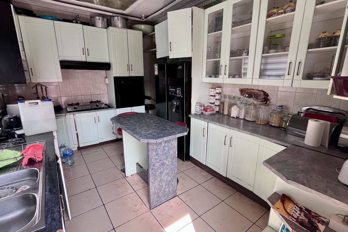 A functional kitchen featuring light-colored cabinetry, laminate countertops, a gas hob, and a double basin sink, with tiled flooring and backsplash throughout.