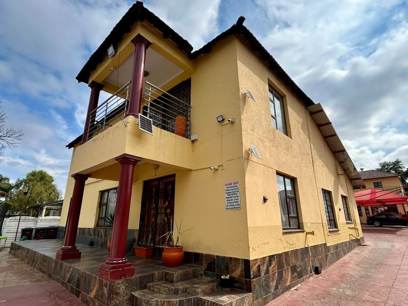 Front elevation of a two-story guest house featuring a covered balcony, tiled base detailing, and paved driveway access.