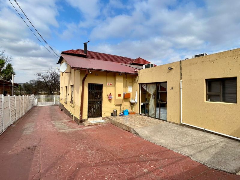 Rear exterior view of the guest house featuring a paved driveway, metal roofing, security gate, and sliding door access.
