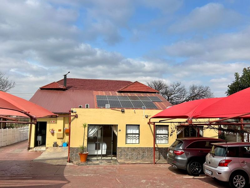 Front exterior view of the guest house featuring a paved driveway, multiple shade cloth carports, and solar panels installed on the tiled roof.