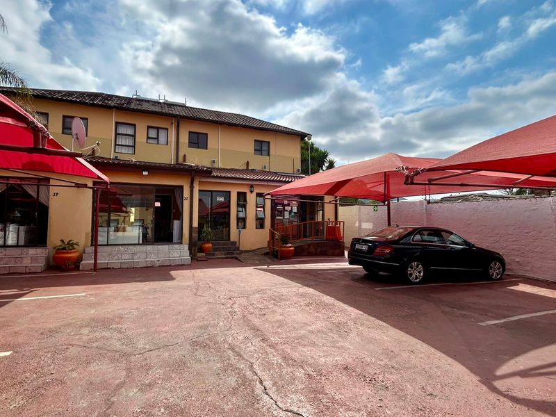 Exterior view of the guest house entrance featuring a paved parking area with shade cloth carports and multi-level building facade.
