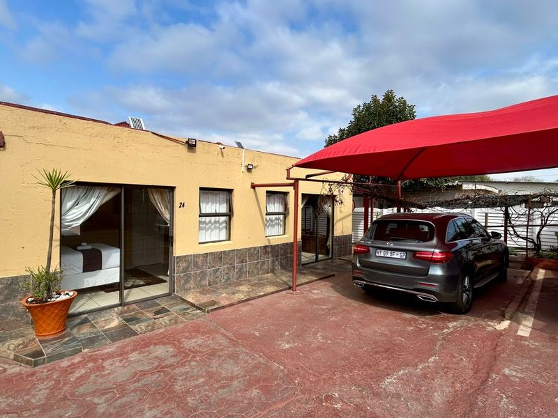 Front exterior view of the guest house featuring a paved driveway, shade sail carport, and sliding door access to the units.