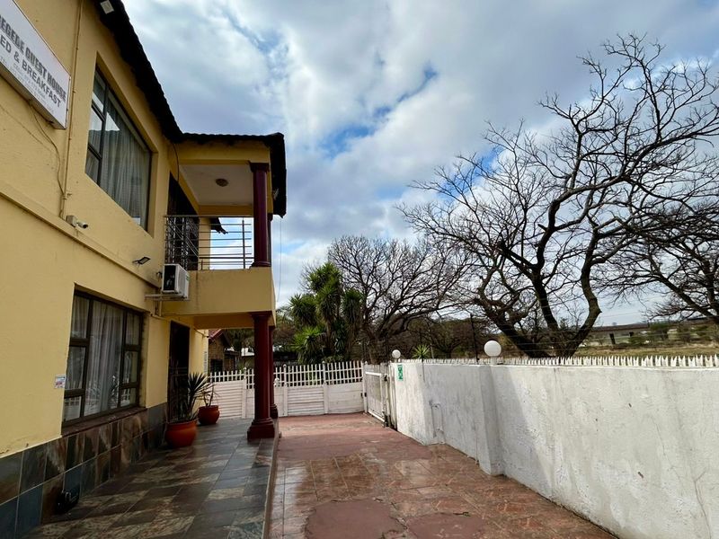 Exterior view of the guest house featuring a tiled patio, balcony, and secure perimeter wall with gated access.