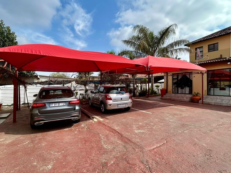 Exterior view of the guest house entrance featuring a large red shade cloth carport and paved driveway area.