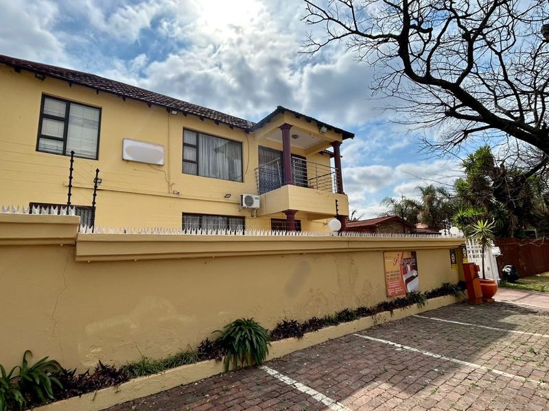 Front exterior view of a two-story guest house featuring a paved driveway, perimeter wall with electric fencing, and a balcony.