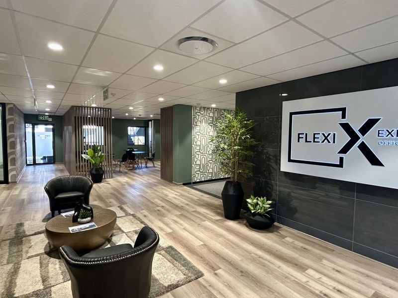 Modern office reception area featuring wood-look laminate flooring, a contemporary feature wall with signage, and a suspended ceiling with recessed lighting.