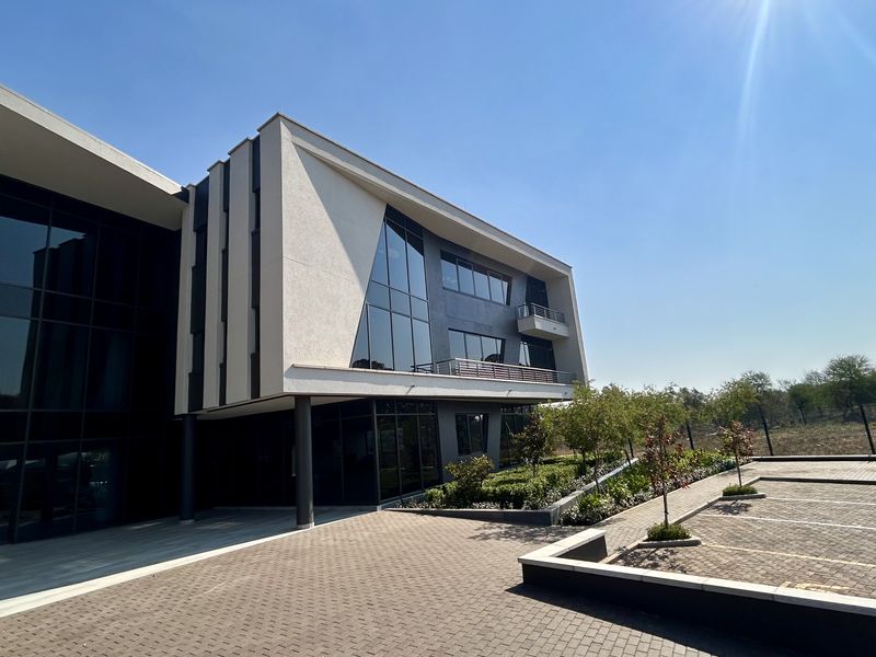 Modern multi-story office building featuring a glass curtain wall, paved parking area, and integrated balcony design.