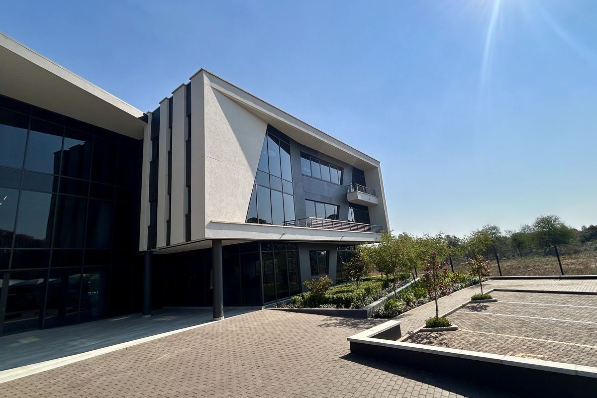 Modern multi-story office building featuring a glass curtain wall, paved parking area, and integrated balcony design.