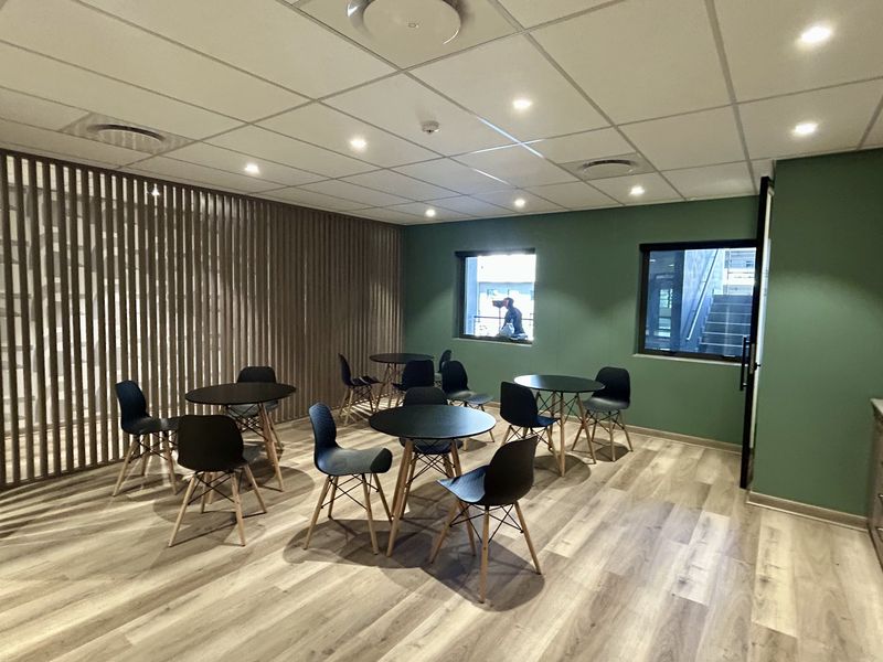 Modern office break-out area featuring wood-look flooring, a decorative timber slat partition, recessed ceiling lighting, and built-in storage cabinetry.