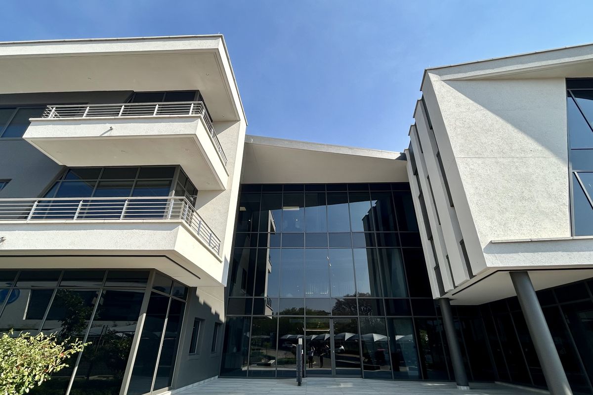 Modern office building exterior featuring a prominent glass curtain wall entrance, multi-level balconies with metal railings, and a clean, contemporary architectural design.