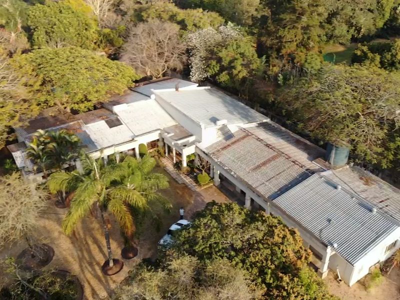 Aerial view of a small holding property featuring a large structure with a corrugated metal roof, mature trees, and a water storage tank.