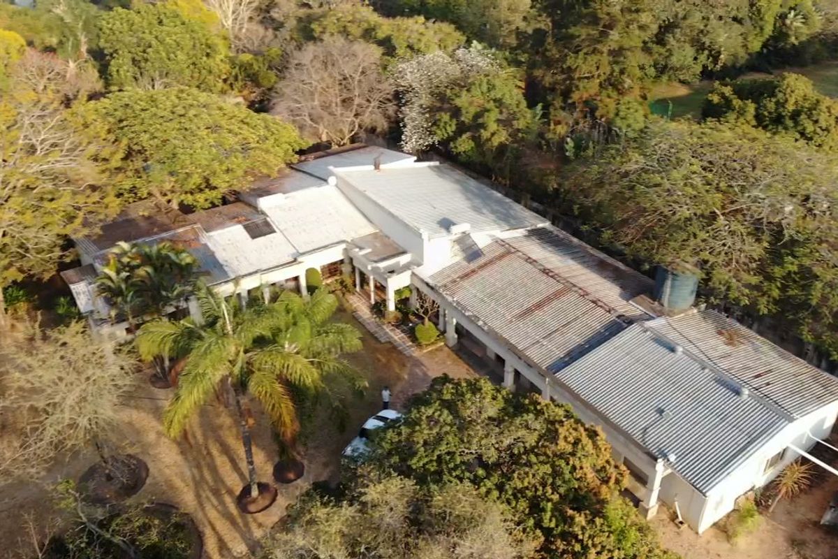 Aerial view of a small holding property featuring a large structure with a corrugated metal roof, mature trees, and a water storage tank.