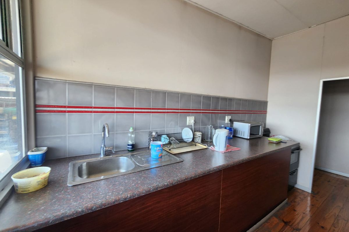A functional kitchen area featuring a stainless steel sink, laminate countertops, tiled backsplash, and timber flooring, suitable for industrial or office utility use.