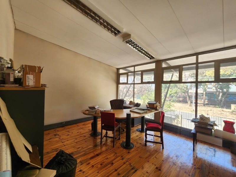 A functional office space featuring large windows providing natural light, timber flooring, and overhead fluorescent lighting, suitable for a professional workspace.