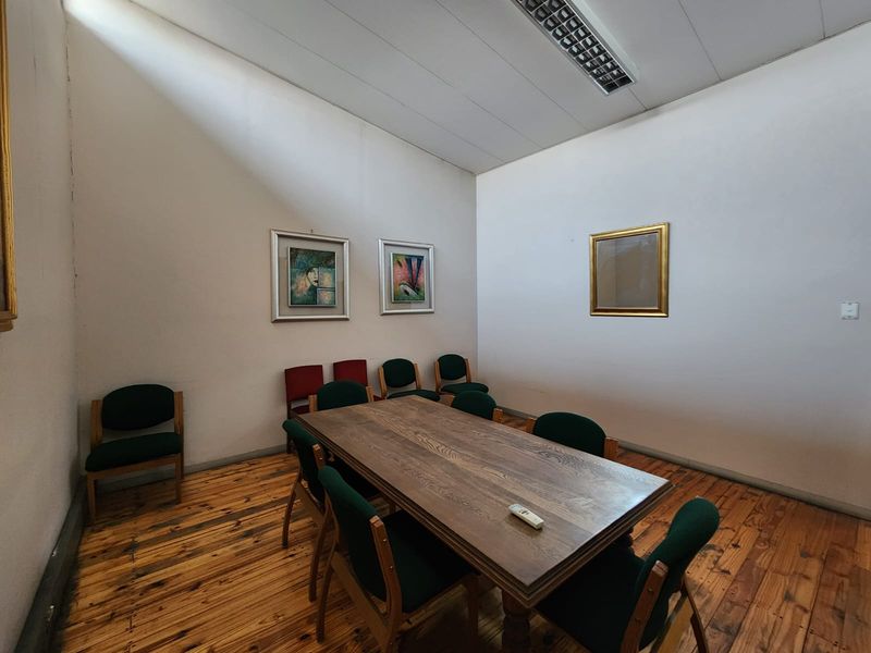 A functional office space featuring timber flooring and a high ceiling with integrated fluorescent lighting.