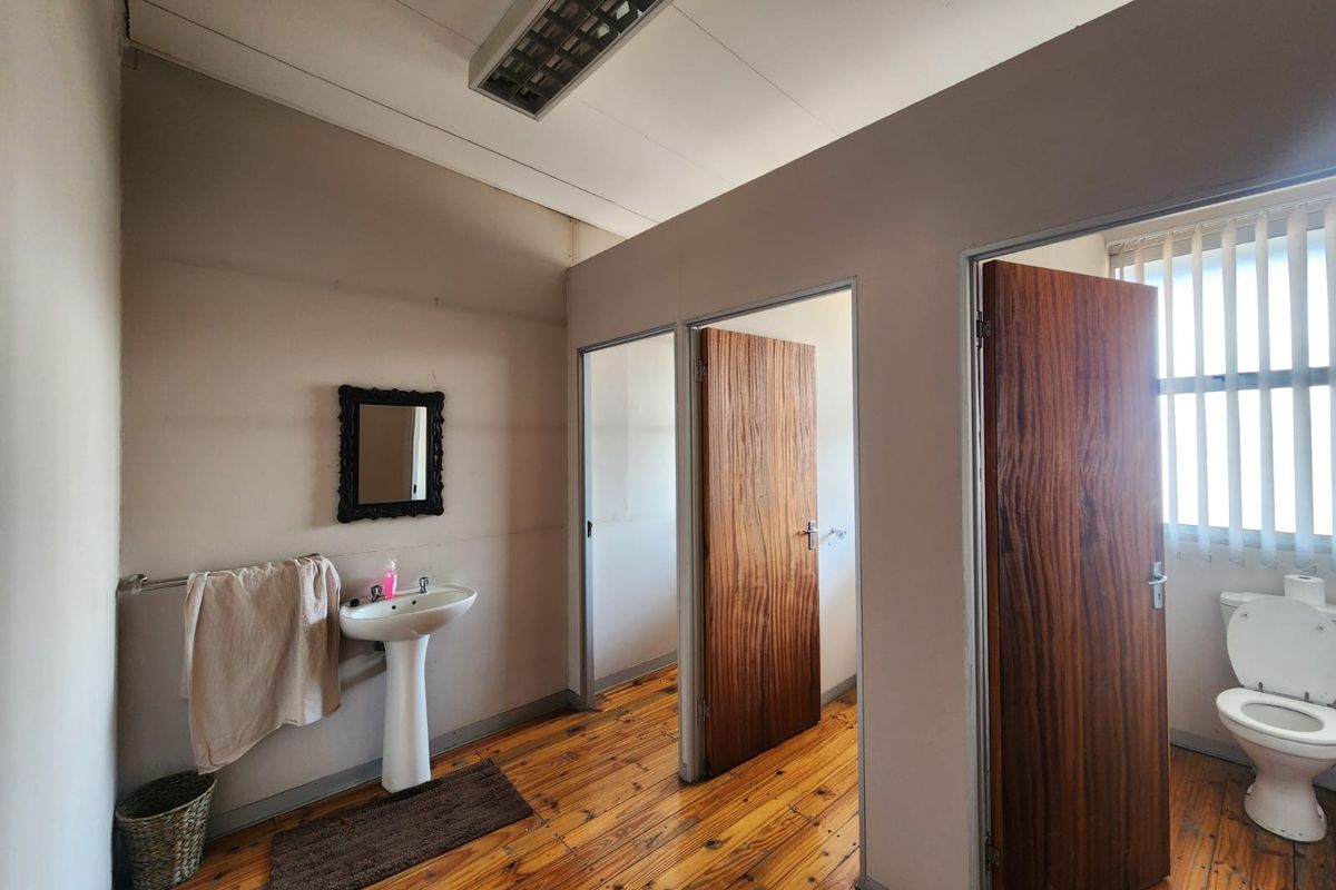 Functional bathroom featuring a pedestal sink, toilet, timber flooring, and natural light through venetian blinds.
