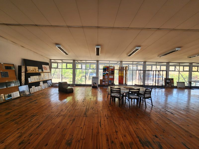 Spacious open-plan industrial area featuring polished timber flooring, extensive natural light from large glass windows, and functional overhead strip lighting.