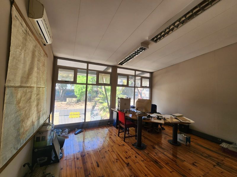 A functional office space featuring timber flooring, large windows providing natural light, air conditioning, and overhead fluorescent lighting.