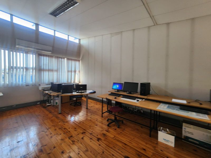 A functional office space featuring polished hardwood flooring, clerestory windows for natural light, vertical blinds, and a wall-mounted air conditioning unit.