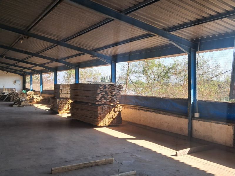 A spacious industrial utility area featuring a steel frame structure, corrugated metal roofing, and concrete flooring, suitable for storage or workshop use.