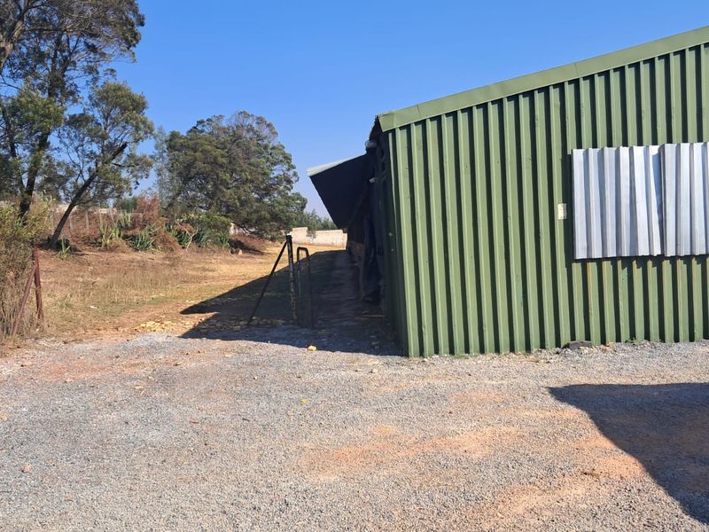 Rear view of an industrial corrugated metal warehouse building with a gravel yard and perimeter fencing.
