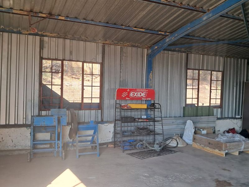 Industrial utility space featuring corrugated metal walls, exposed steel roof trusses, and concrete flooring, suitable for workshop or storage use.