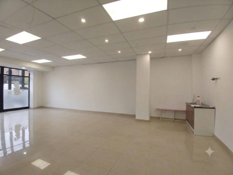 A bright, open-plan retail space featuring a suspended ceiling with recessed lighting, polished tiled floors, and a glass storefront entrance.