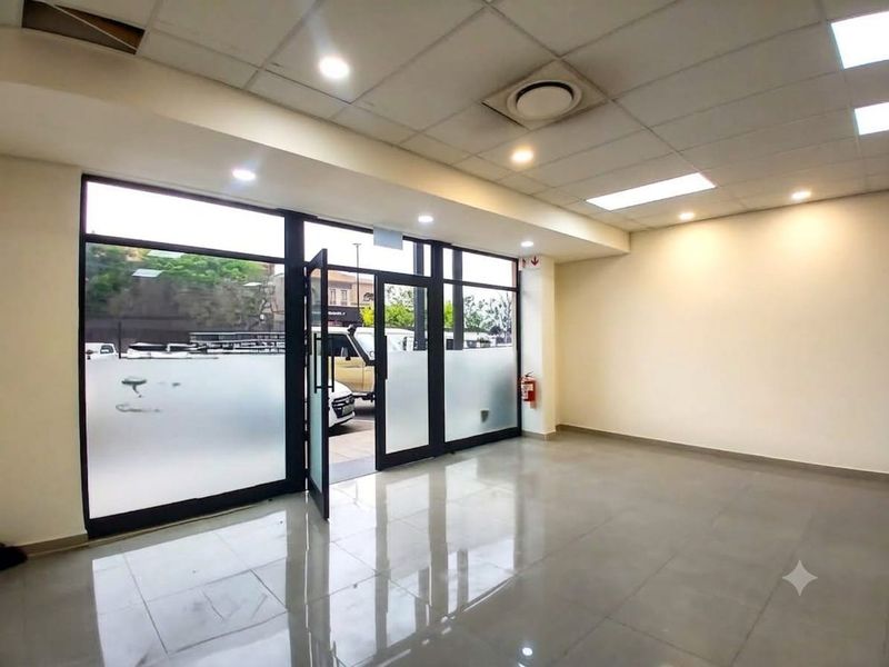 A bright, open-plan retail entrance area featuring tiled flooring, a suspended ceiling with recessed lighting, and large glass frontage with aluminium frames.