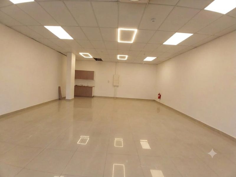 Spacious open-plan retail or office area featuring tiled flooring, recessed lighting, a suspended ceiling, and a small kitchenette corner.