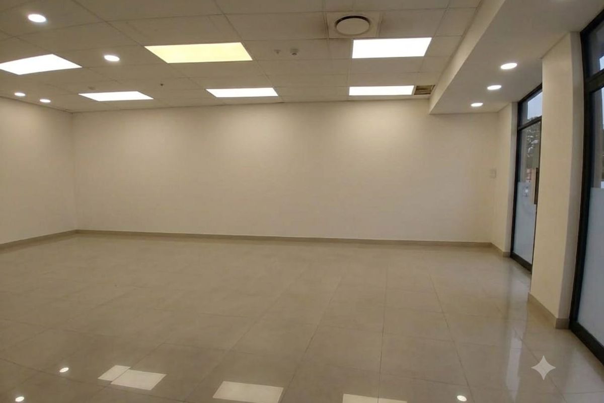 A spacious, empty open-plan retail unit featuring polished tiled flooring, a suspended ceiling with recessed lighting, and a glass entrance door.