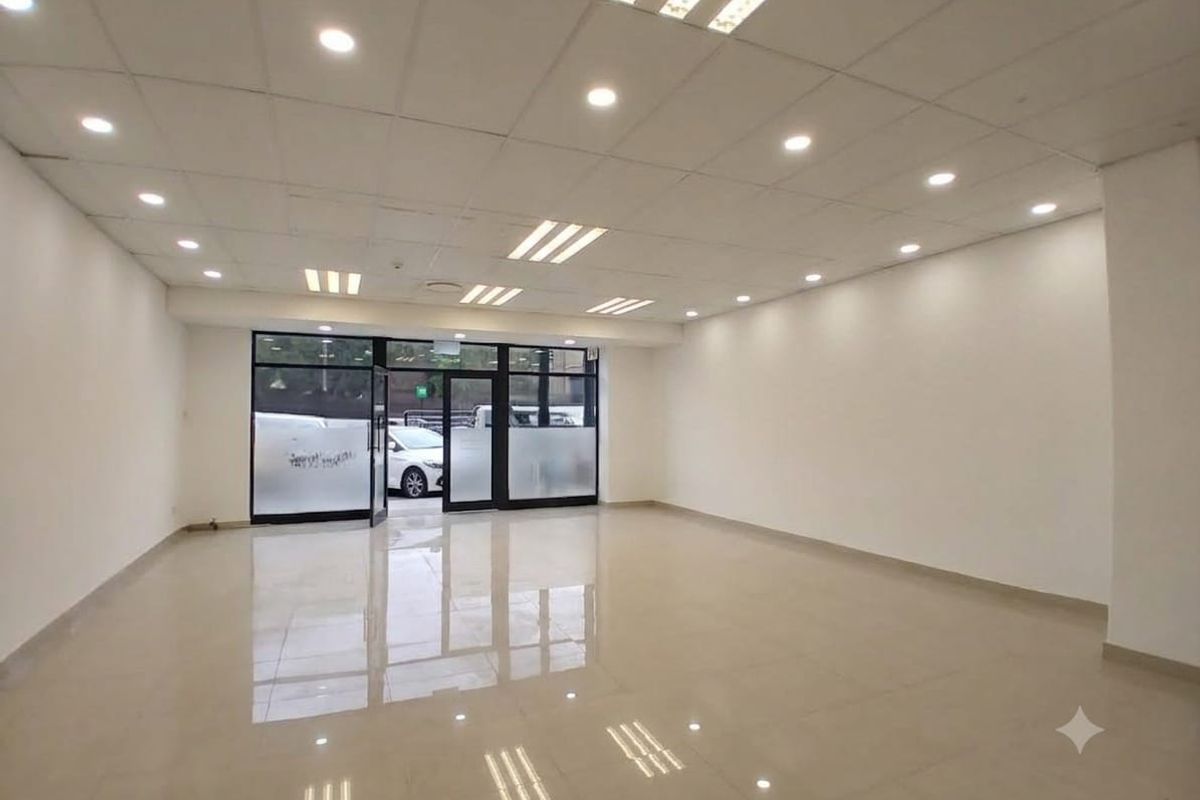 A spacious, empty open-plan retail unit featuring polished tiled floors, a suspended ceiling with recessed lighting, and a large glass storefront entrance.