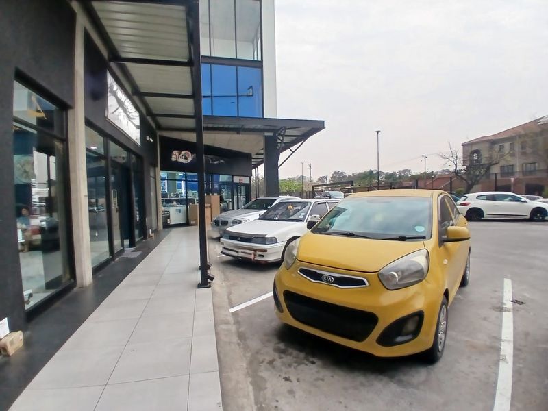 Exterior view of a modern retail storefront featuring a tiled walkway, glass facade, and dedicated parking area.
