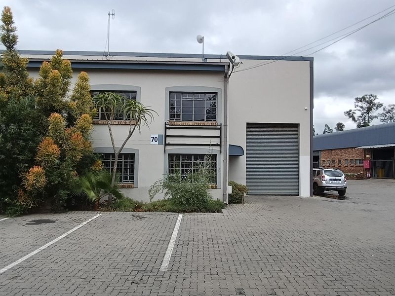 Front elevation of an industrial property featuring a roller shutter door, paved parking area, and established landscaping.