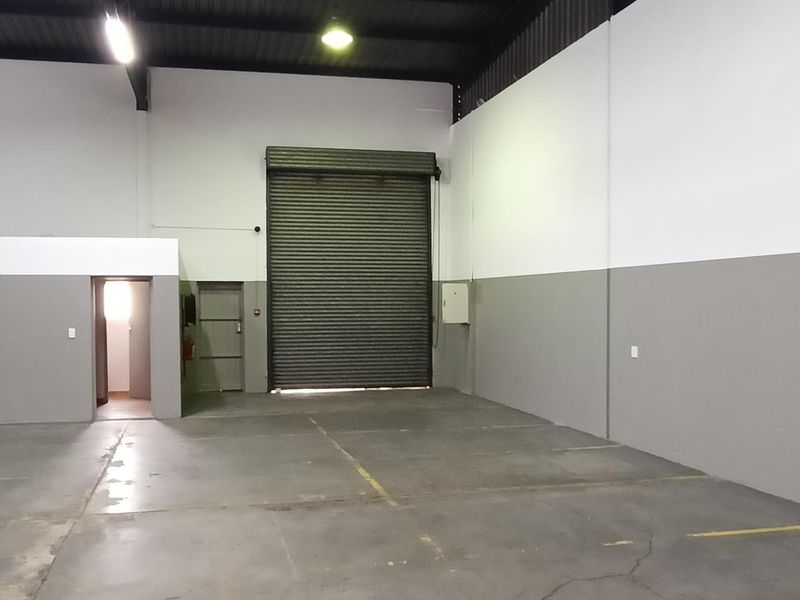 Spacious industrial warehouse unit featuring high ceilings, exposed steel roof structure, concrete flooring, and a large roller shutter door for easy access.