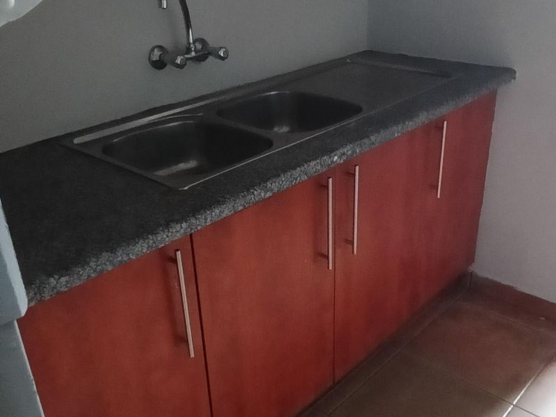 A functional scullery area featuring dark laminate cabinetry, a granite countertop with a double bowl stainless steel sink, and ceramic floor tiles.