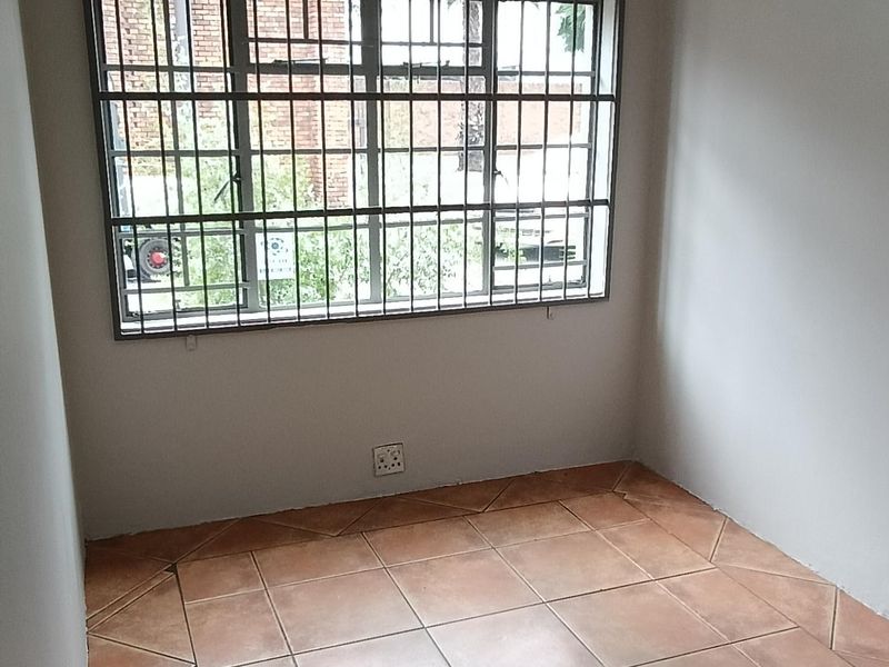 A clean, empty office space featuring tiled flooring, a fluorescent light fixture, and a window secured with metal bars.