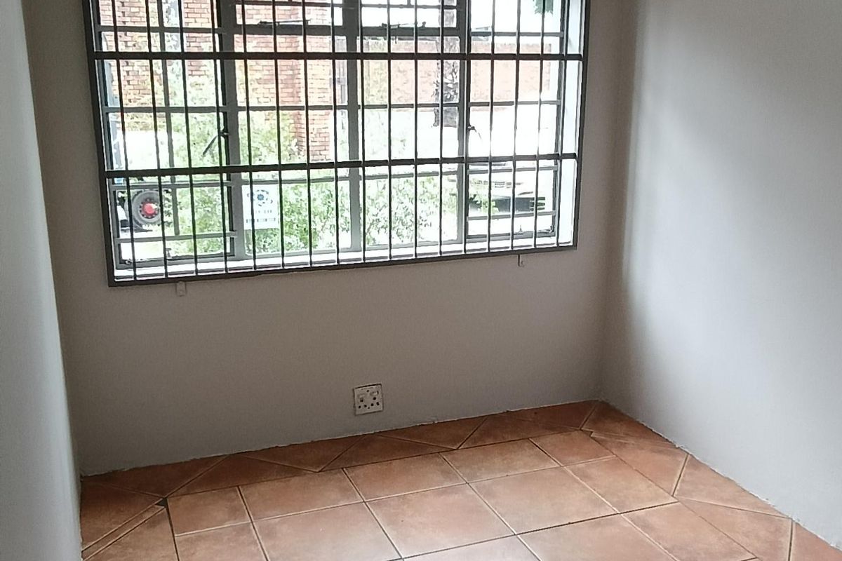 A clean, empty office space featuring tiled flooring, a fluorescent light fixture, and a window secured with metal bars.