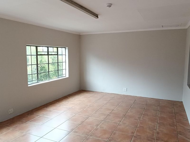 A clean, empty office space featuring neutral walls, ceramic tiled flooring, and large steel-framed windows providing natural light.
