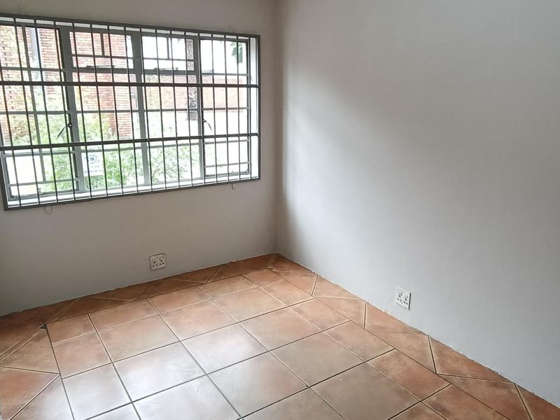 A clean, empty office space featuring tiled flooring, a window with security bars, and a wall-mounted fire extinguisher.